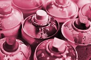 A lot of used spray cans of paint close-up. Dirty and smeared cans for drawing graffiti. Image toned in Viva Magenta, color of the 2023 year photo