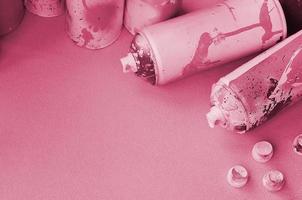 Some used pink aerosol spray cans and nozzles with paint drips lies on a blanket of soft and furry light pink fleece fabric. Image toned in Viva Magenta, color of the year photo