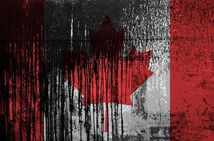 Canada flag depicted in paint colors on old and dirty oil barrel wall closeup. Textured banner on rough background photo