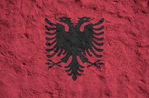 Albania flag depicted in bright paint colors on old relief plastering wall. Textured banner on rough background photo