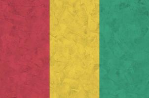 Guinea flag depicted in bright paint colors on old relief plastering wall. Textured banner on rough background photo