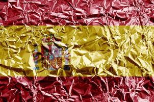 Spain flag depicted in paint colors on shiny crumpled aluminium foil closeup. Textured banner on rough background photo