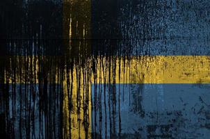 Sweden flag depicted in paint colors on old and dirty oil barrel wall closeup. Textured banner on rough background photo
