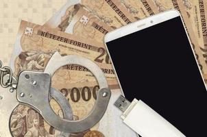 2000 Hungarian forint bills and smartphone with police handcuffs. Concept of hackers phishing attacks, illegal scam or malware soft distribution photo