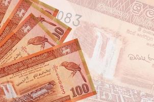 Los billetes de 100 rupias de Sri Lanka se encuentran apilados en el fondo de un gran billete semitransparente. fondo de negocios abstracto foto