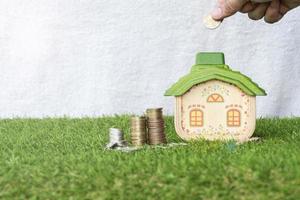 Mock up house with coins stack on grass floor and hand putting money coin. photo