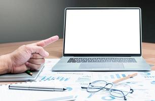 Hand pointing finger to mock up sales summary slide show presentation on display laptop with pen ,glasses and paper work on table in meeting room photo
