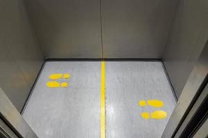 Social distancing for COVID-19 with yellow footprint sign in public elevator photo