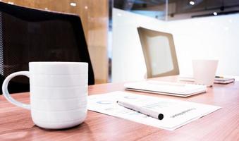 Coffee cup ,paperwork and notebook on table with two black armchairs in meeting room photo