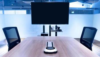 micrófono inalámbrico portátil en la mesa de reuniones central con televisión de pantalla en blanco en la sala de reuniones de videoconferencia foto