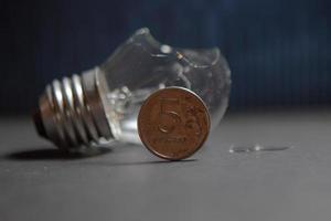 Broken light bulb with pieces of glass and 5 Russian 5 ruble coin. Concept of electricity prices and the electricity crisis in Russia and Europe photo