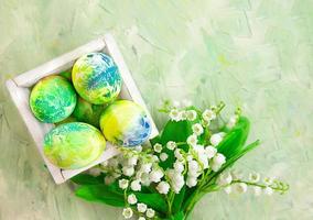 Colored eggs in box with lilies of the valley on mint green abstract background. Easter. Copy space photo
