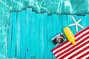 Red and white striped towel with camera, yellow bottle, starfish on blue wooden boards, pier. Pool, beach, sea. Vertical, horizontal. Vacation, travel, relaxation. Copy space photo