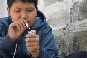 Boy learning to smoke by himself in the area behind the school fence which is a hidden place for people, bad influence of secondary school or junior high school life, addiction. photo