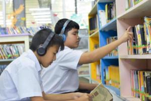 Soft fucus of two asian boy students are listening media, reading and consulting about favourite book at library of school photo