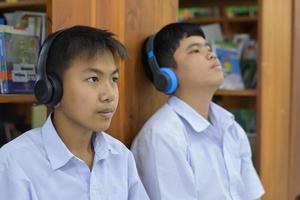 Soft fucus of two asian boy students are listening media, reading and consulting about favourite book at library of school photo