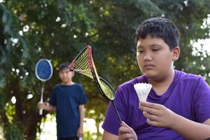un joven asiático sostiene una raqueta de bádminton de marco roto en la mano tristemente mientras juega bádminton con su amigo fuera de la casa, concepto de bádminton al aire libre, enfoque suave y selectivo. foto