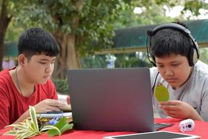 Young Asian boys doing homework and do the reports about various species of tropical forests by using laptops, magnifiers, notebooks, pocket binoculars and tablets, mockup laptop concept. photo