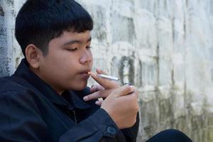 Boy learning to smoke by himself in the area behind the school fence which is a hidden place for people, bad influence of secondary school or junior high school life, addiction. photo