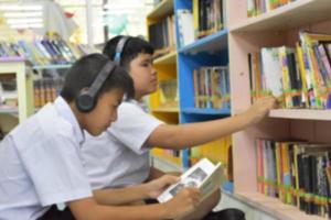 Soft fucus of two asian boy students are listening media, reading and consulting about favourite book at library of school photo