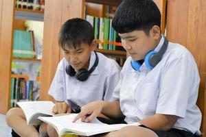 el fucus suave de dos estudiantes asiáticos está escuchando los medios, leyendo y consultando sobre su libro favorito en la biblioteca de la escuela foto