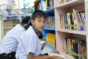 Soft fucus of two asian boy students are listening media, reading and consulting about favourite book at library of school photo