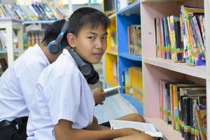Soft fucus of two asian boy students are listening media, reading and consulting about favourite book at library of school photo