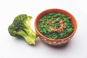 chutney o pasta de brócoli fresco, puré en el recipiente con trozos crudos foto