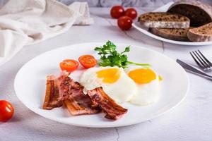Fried eggs and bacon, tomatoes and parsley on a plate on the table. Homemade breakfast. photo