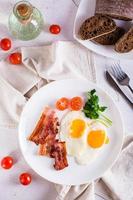 Homemade breakfast fried bacon and eggs, tomatoes and greens on a plate. Top and vertical view photo