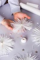 Children's hands hold a paper snowflake with a thread and a bead. Handmade decor. Vertical view photo