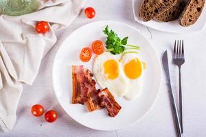 Fried eggs and bacon, tomatoes and parsley on a plate on the table. Homemade breakfast. Top view photo