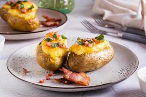 Twice baked potatoes with bacon and cheese on a plate on the table. Homemade dinner.