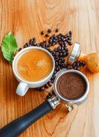 Top view of Espresso coffee cup and equipment of barista coffee tool portafilter with tamper and dark roasted coffee beans with green coffee leaf  on wooden table photo