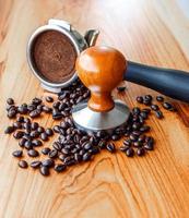 Equipment of barista coffee tool portafilter with tamper and dark roasted coffee beans on wooden table in a coffee shop photo