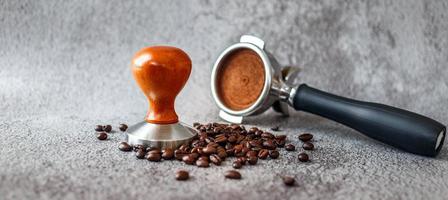 Equipment in a coffee shop of barista coffee tool portafilter with tamper and dark roasted coffee beans on gray background photo