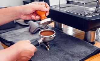 Barista cafe making coffee with manual presses ground coffee using tamper on the wooden counter bar at the coffee shop photo