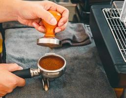 Barista cafe making coffee with manual presses ground coffee using tamper on the wooden counter bar at the coffee shop photo