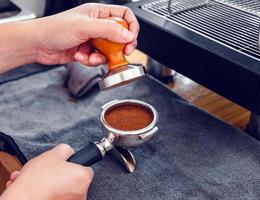 Barista cafe making coffee with manual presses ground coffee using tamper on the wooden counter bar at the coffee shop photo