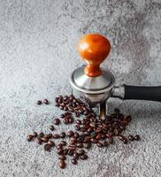 Equipment in a coffee shop of barista coffee tool portafilter with tamper and dark roasted coffee beans on gray background photo