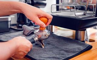 Barista cafe making coffee with manual presses ground coffee using tamper on the wooden counter bar at the coffee shop photo