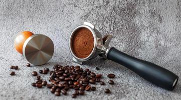 equipo en una cafetería de portafiltro de herramientas de café barista con tamper y granos de café tostados oscuros sobre fondo gris foto