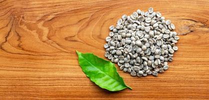 Top view of unroasted raw coffee beans or Dried green coffee beans and green coffee leaf  on wooden background photo