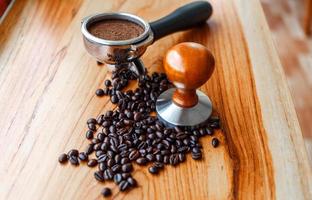 Equipment in a coffee shop of barista coffee tool portafilter with tamper and dark roasted coffee beans on wooden background photo