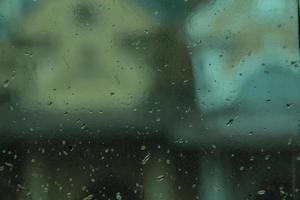 una escena de lluvia de gotas en la ventana con una casa borrosa en el fondo. gotas de condensación en el vidrio sudoroso. ventana mojada foto