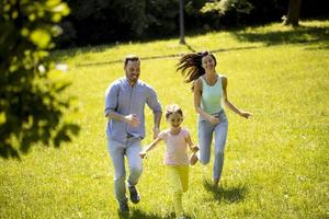 Happy young family with cute little daughter running in the park on a sunny day photo