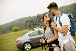 Smiling young couple walking with backpacks on the green hills photo