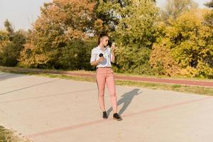 Happy young woman with coffee listening music on smartphone and walking on promenade photo