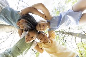 Group of asian and caucasian happy kids huddling, looking down at camera and smiling photo