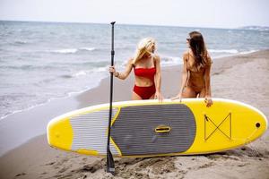 Dos mujeres jóvenes con paddle board en la playa en un día de verano foto